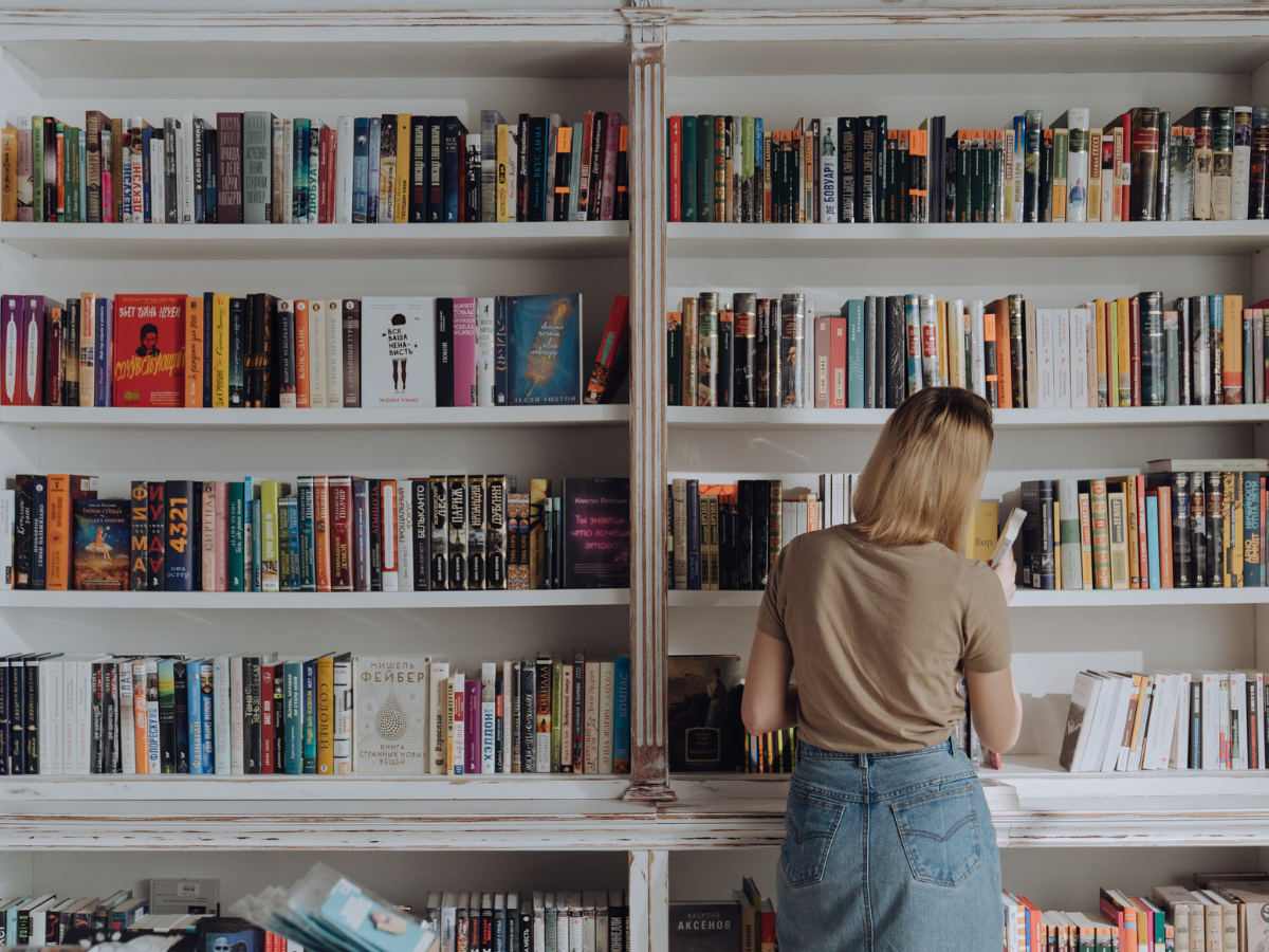 a person looking for a book from a wall bookshelf.
