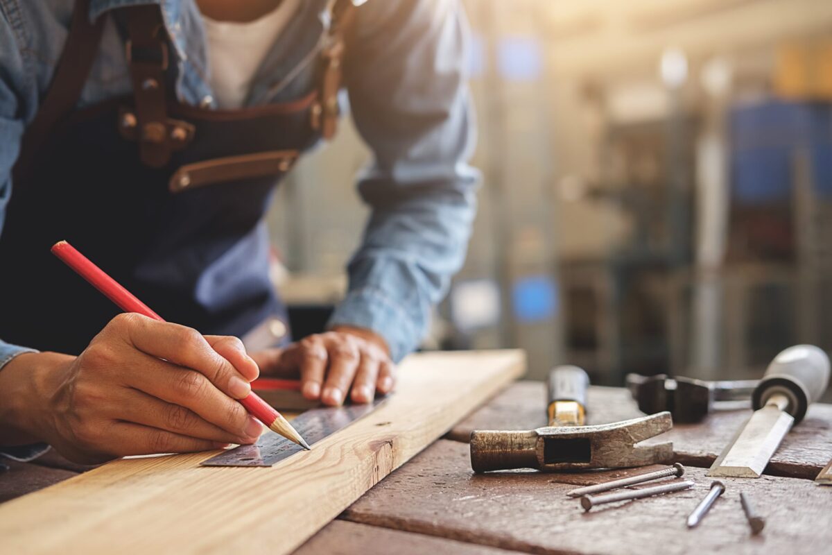 Close up of someone drawing a line on a piece of wood with a ruler.