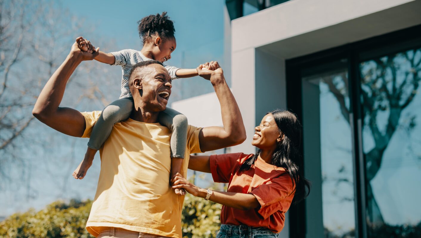 Close of a family laughing with the kid on her dads shoulders.