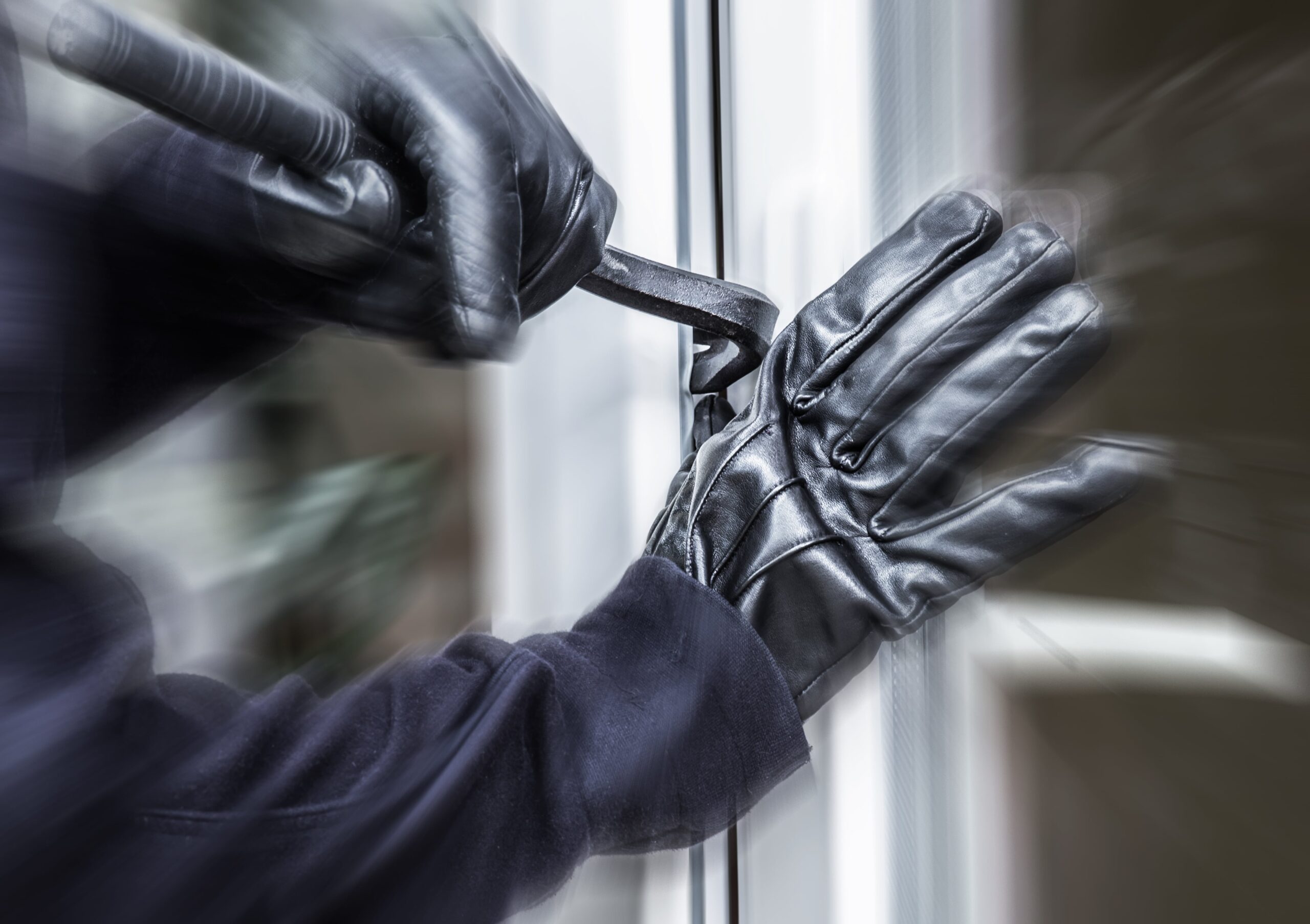 someone with black gloves on breaking into a window with a crowbar.