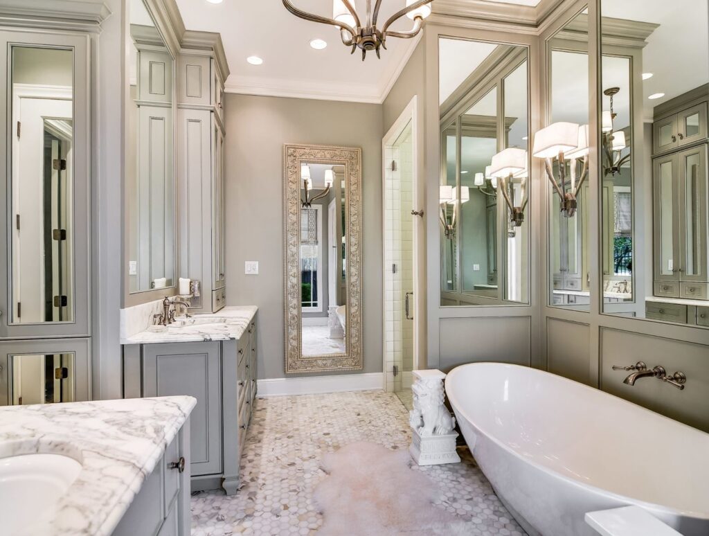 Luxurious bathroom featuring marble countertops and a freestanding tub, with a tall ornate framed mirror concealing a hidden door that blends seamlessly into the wall.
