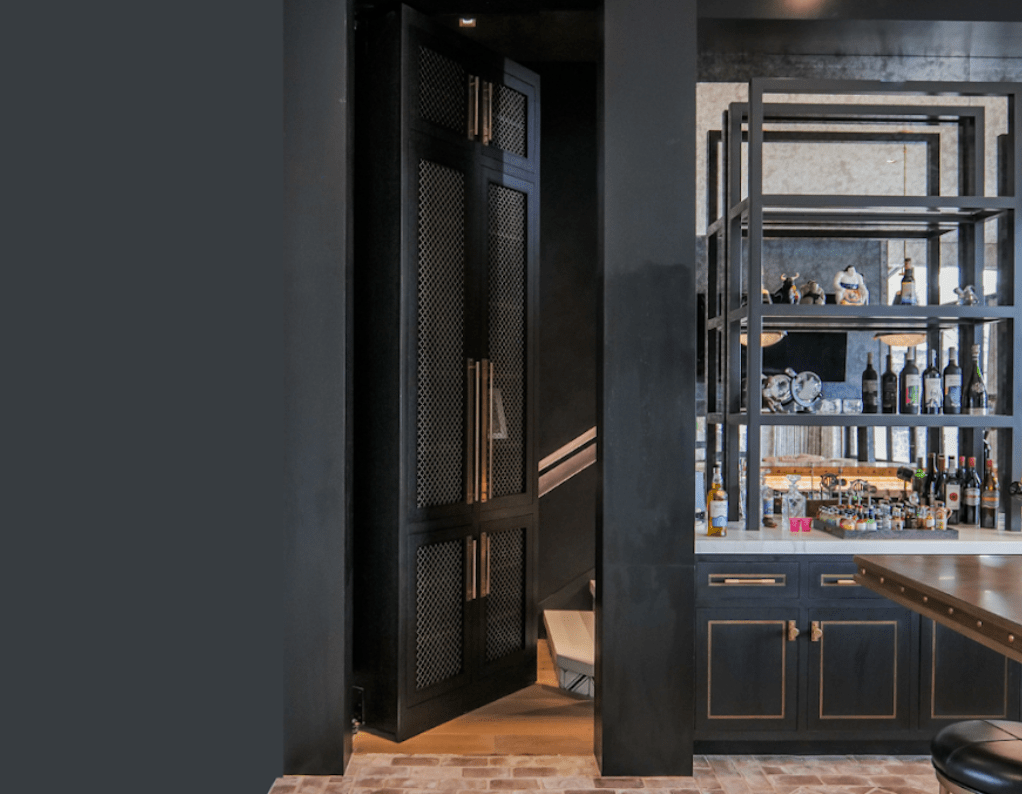 Hidden black metal door with automatic opening seamlessly integrated into a luxury home bar and shelving unit. Hidden door in kitchen designed by Creative Home Engineering.