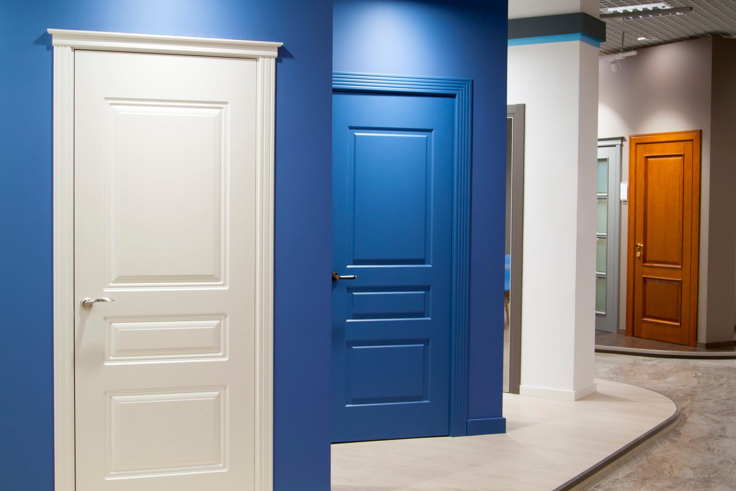 Showroom display of modern interior doors in various colors and finishes, including white, blue, and wood grain styles, arranged along curved walls.