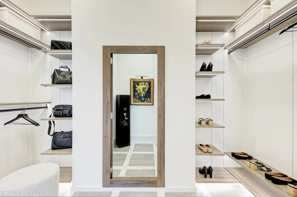 A modern walk-in closet featuring shelves with handbags and shoes, centered around a full-length mirror that doubles as a hidden door. 