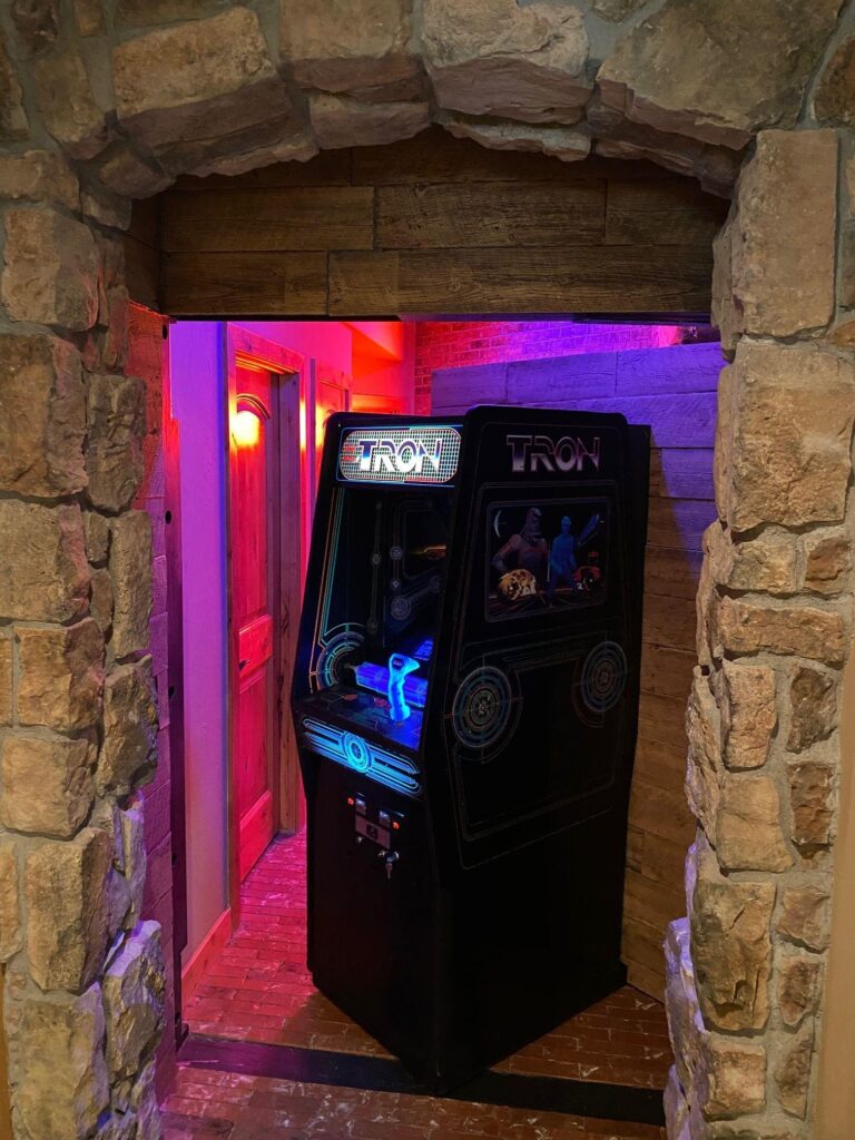 TRON arcade cabinet inside a hidden stone passageway leading to a secret game room.