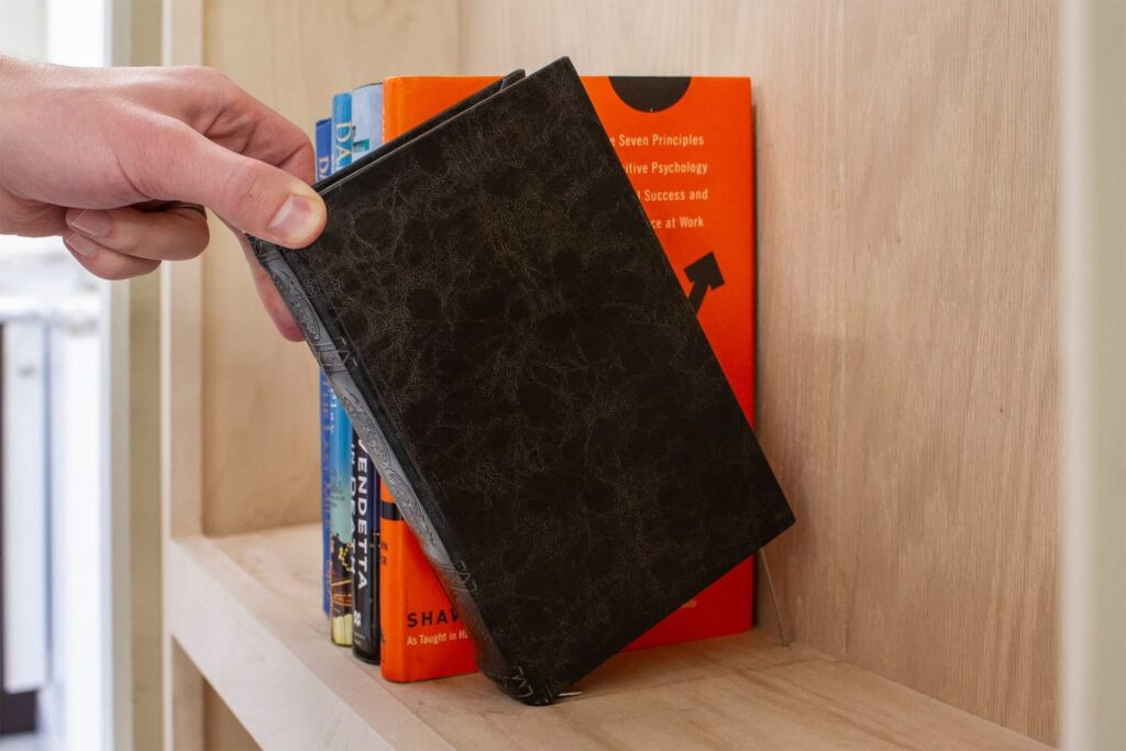 Person using a book latch on a hidden bookcase door to access a concealed room.
